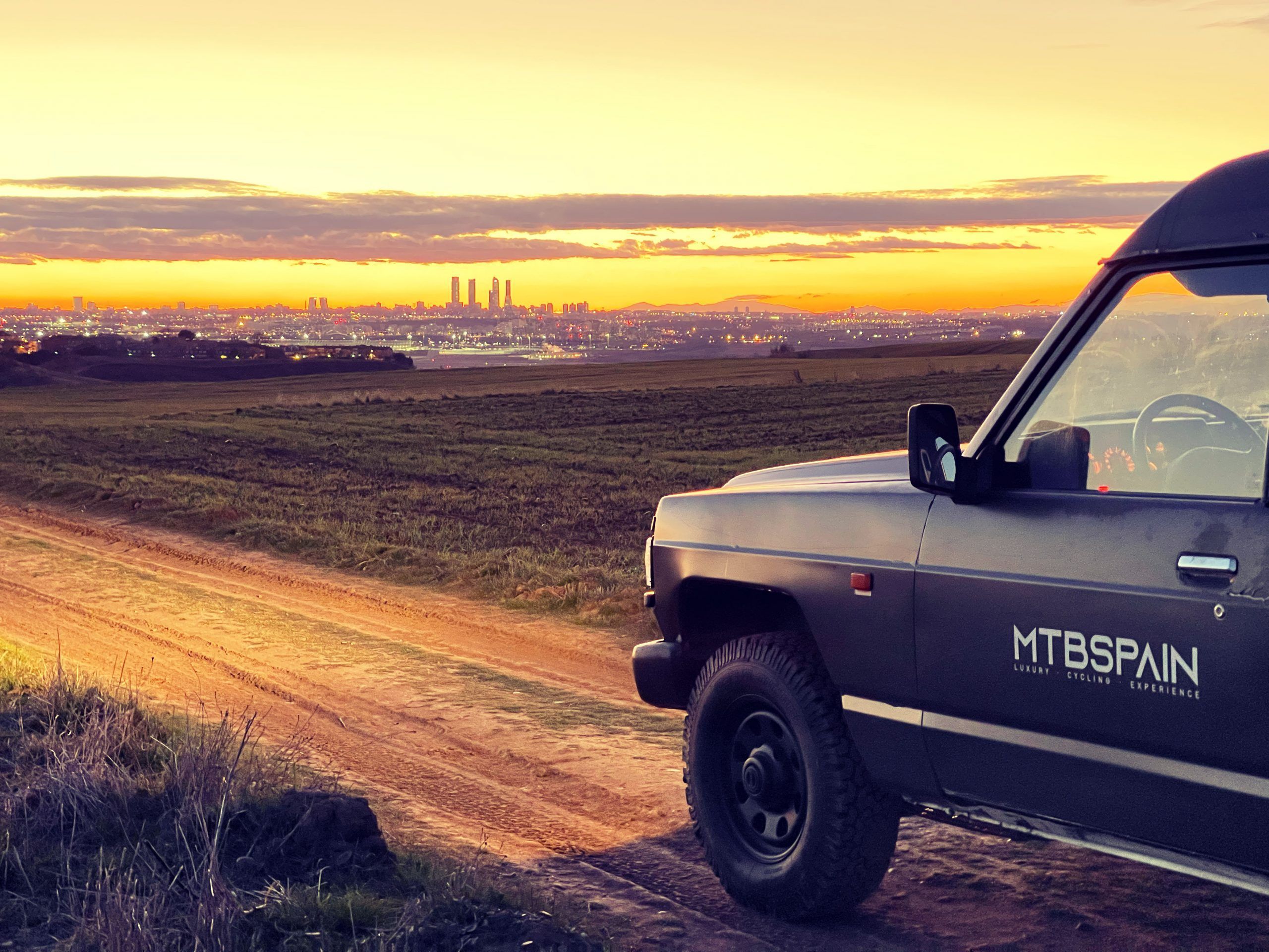 Vehículo 4x4 en una pista de tierra al amanecer, con el perfil de Madrid al fondo