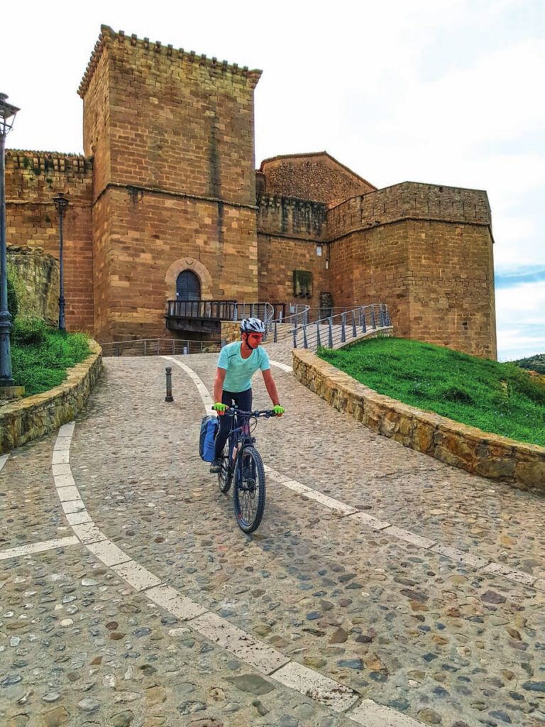 Ciclista con bicicleta de montaña junto a una muralla histórica en una etapa del Camino