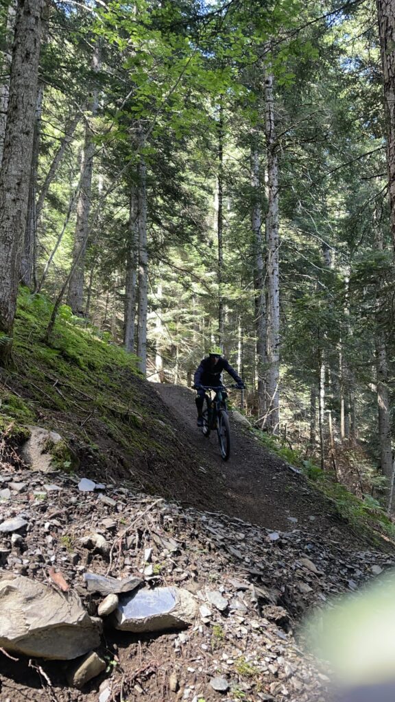 Ciclista de enduro descendiendo un tramo técnico de bosque con casco y protecciones