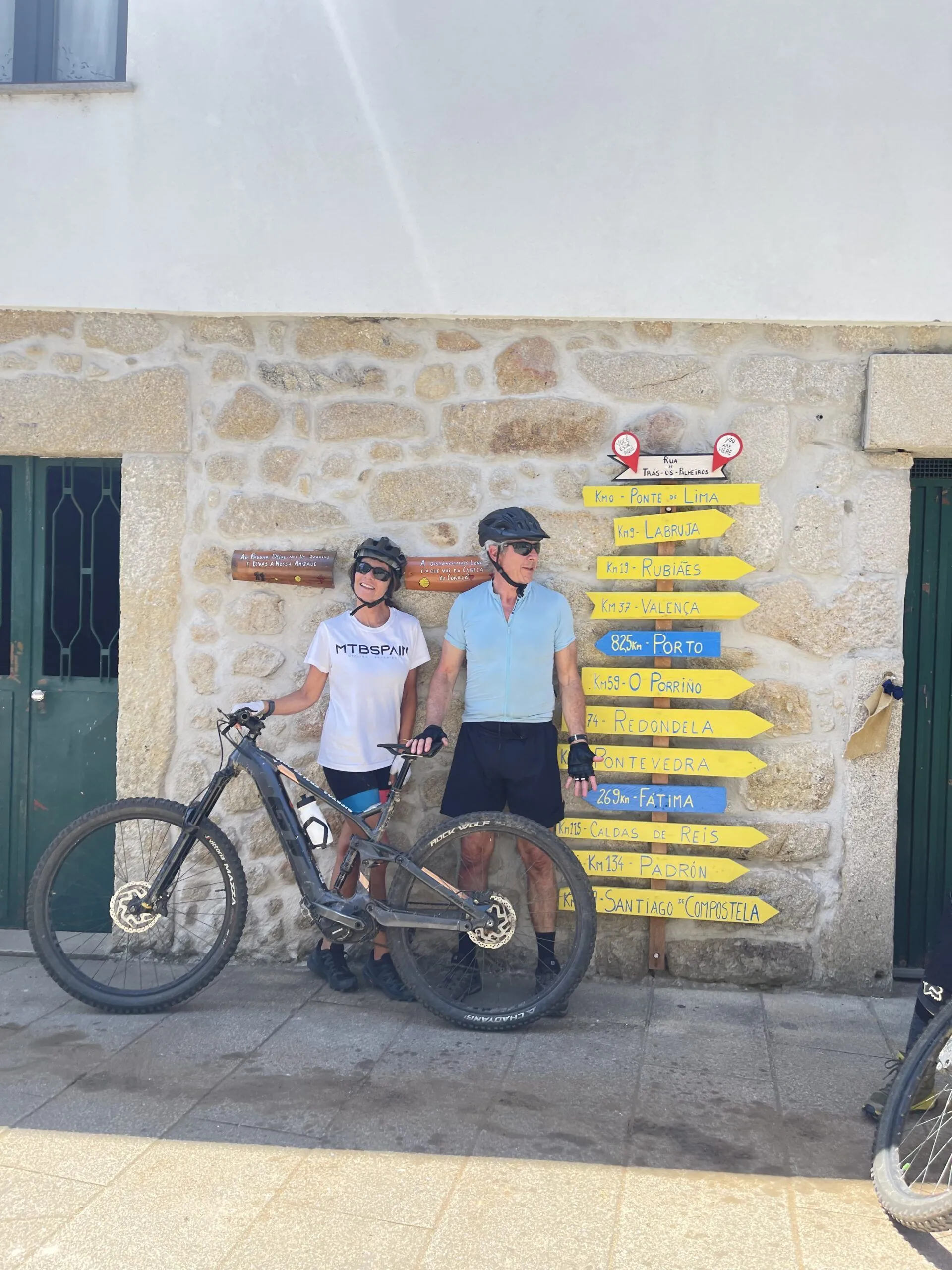 Dos ciclistas con bicicleta eléctrica junto a las señales del Camino de Santiago en Portugal
