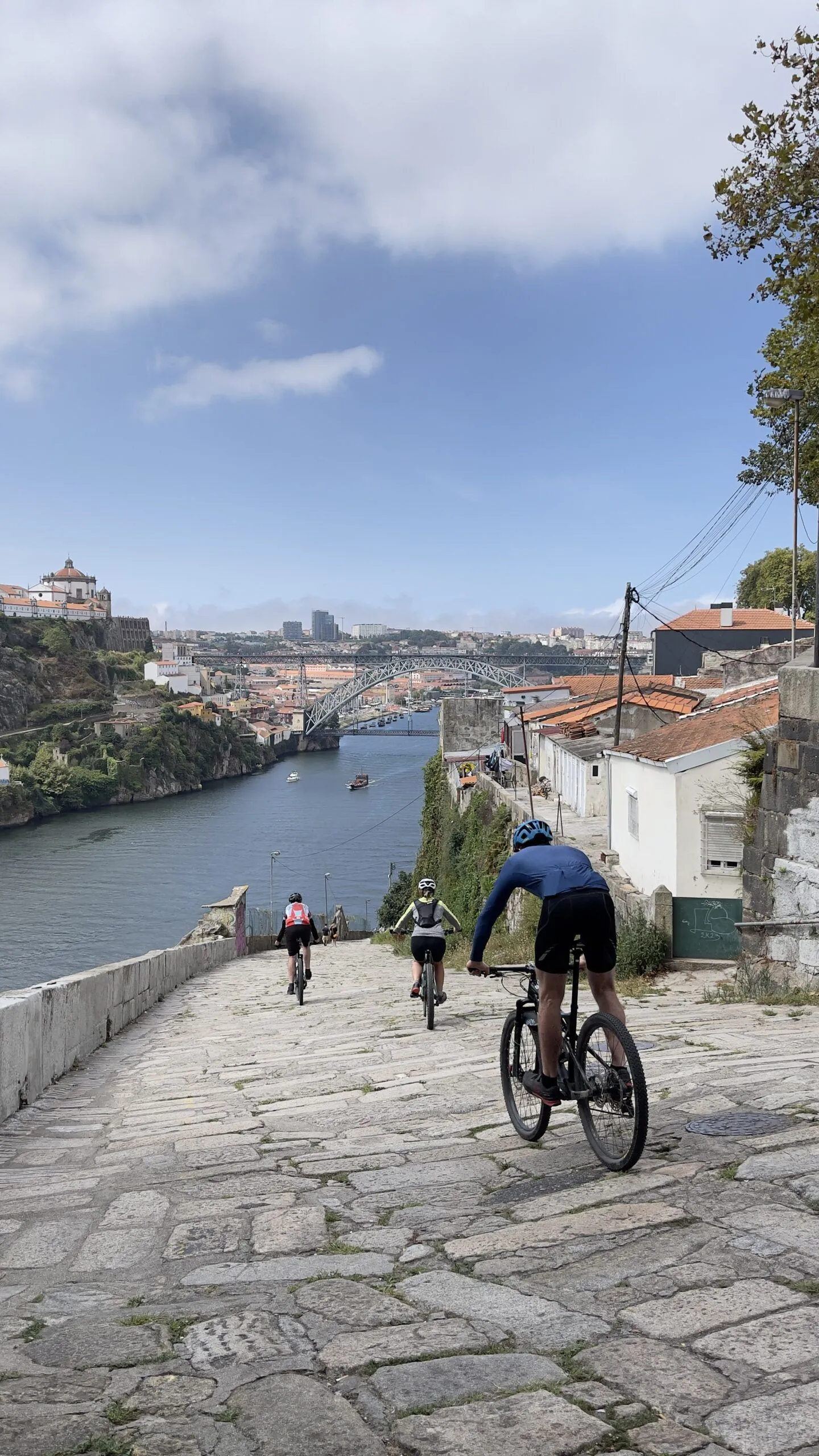 Ciclistas bajando por una calle empedrada de Oporto junto al río Duero en el Camino Portugués